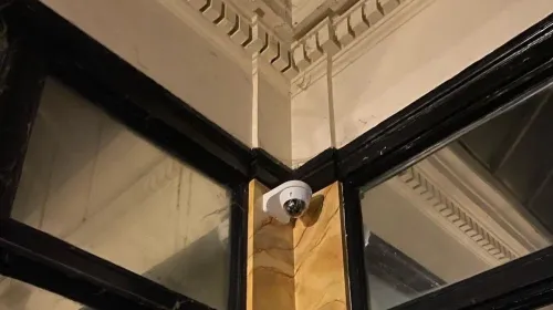 Caméra dôme fixée dans l'angle d'un hall d'immeuble ancien, sous les moulures