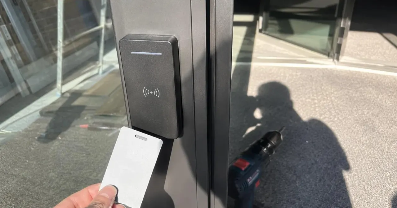 Badge présenté à un lecteur de contrôle d'accès posé sur le montant d'une porte vitrée