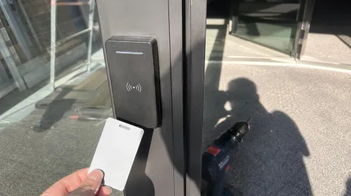 Badge présenté à un lecteur de contrôle d'accès posé sur le montant d'une porte vitrée