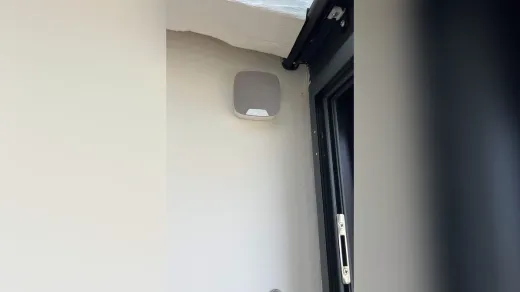 Sirène d'alarme Ajax blanche posée en façade, à côté d'une porte-fenêtre